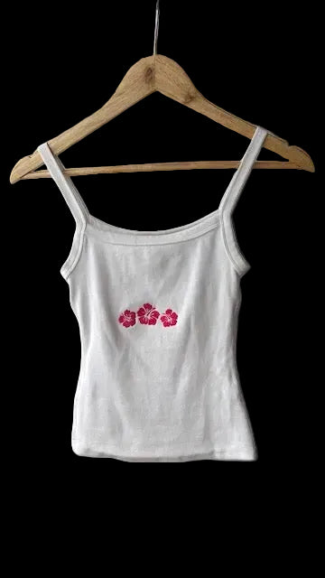 White tank top with dark pink floral hibiscus design on a wooden hanger.